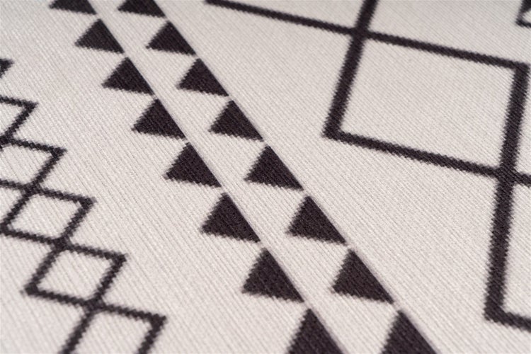 Detailní záběr na koberec s černým geometrickým vzorem trojúhelníků a linií, tkaná textura.