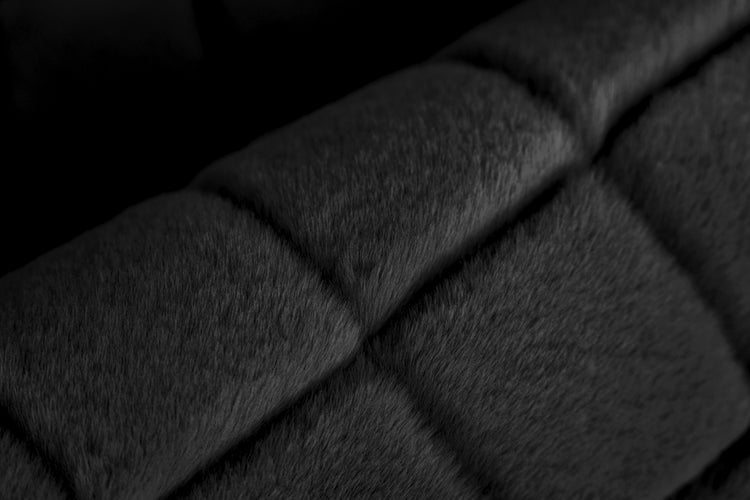 Detailní záběr na měkkou, prošívanou umělou kožešinu v černé barvě.
