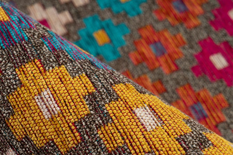 Detailní záběr na tkaný koberec s geometrickým vzorem kilim a hrubou textilní strukturou.