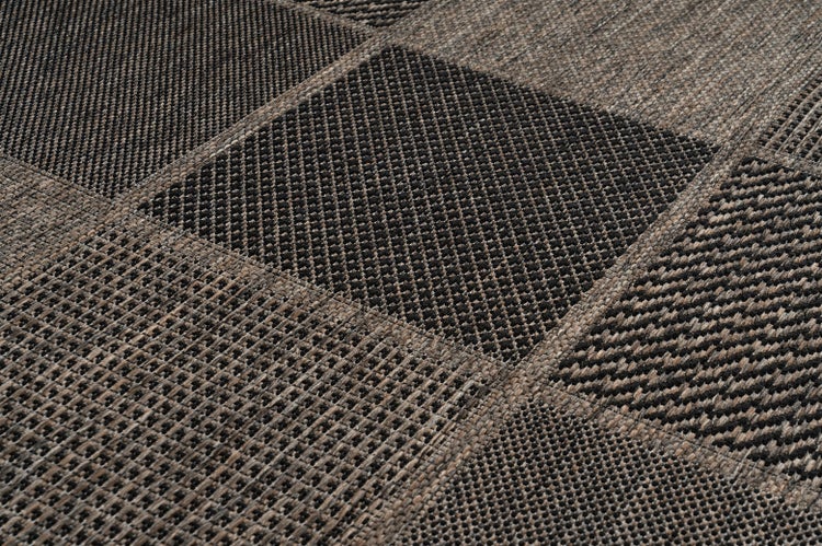 Detailní pohled na tkaný koberec s různými patchworkovými vzory a různými texturami.
