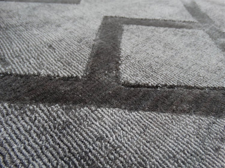 Detailní záběr šedého koberce s geometrickým vzorem a strukturovaným povrchem.