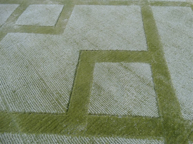 Zelený koberec s geometrickým čtvercovým vzorem a vysokým a nízkým vlasem.