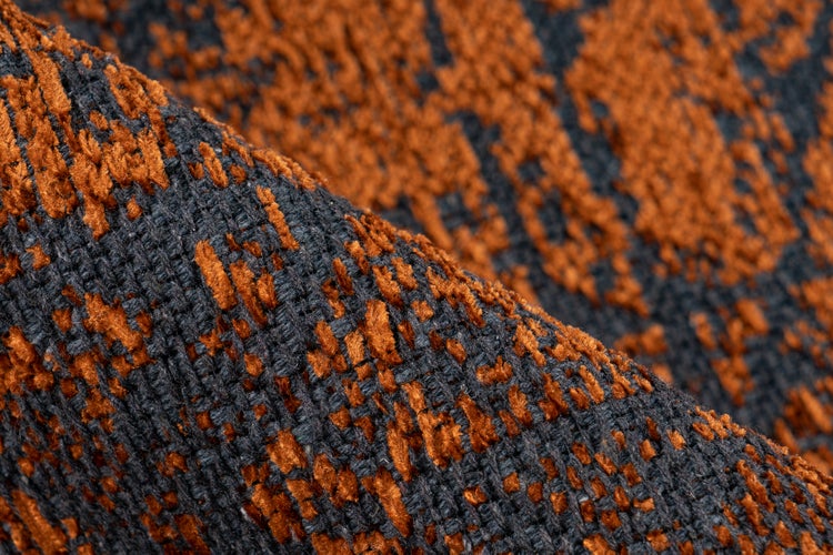 Detailní záběr textury tkaného koberce s oranžovým vzorem na tmavém podkladu.