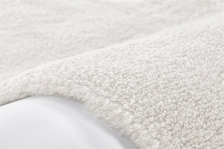 Detailní pohled na huňatou bílou koupelnovou předložku s vysokým vlasem z měkkého materiálu.