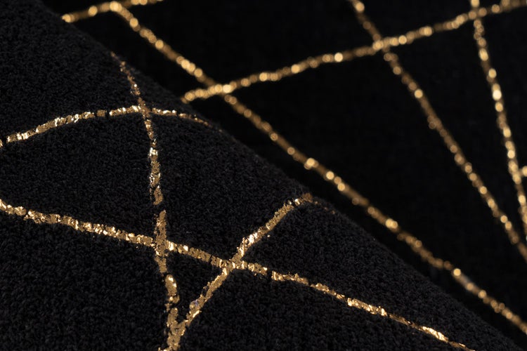 Detailní záběr černé strukturované textilie s geometrickým vzorem zlatých linií.