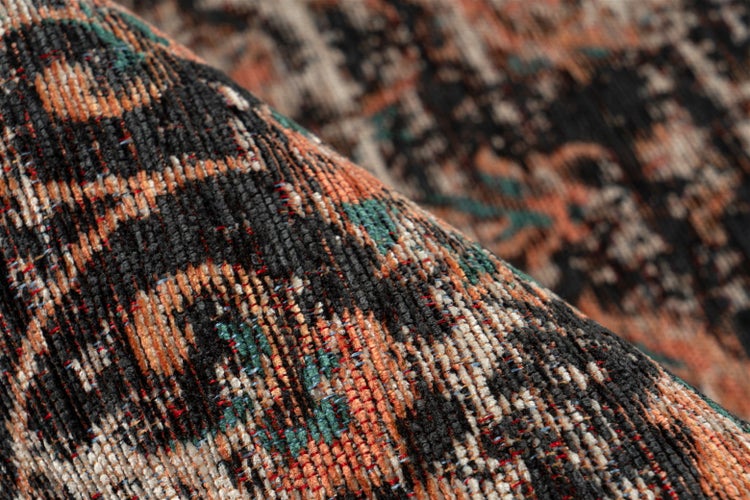 Detail tkaného koberce s vintage vzorem v černé, oranžové a zelené barvě.
