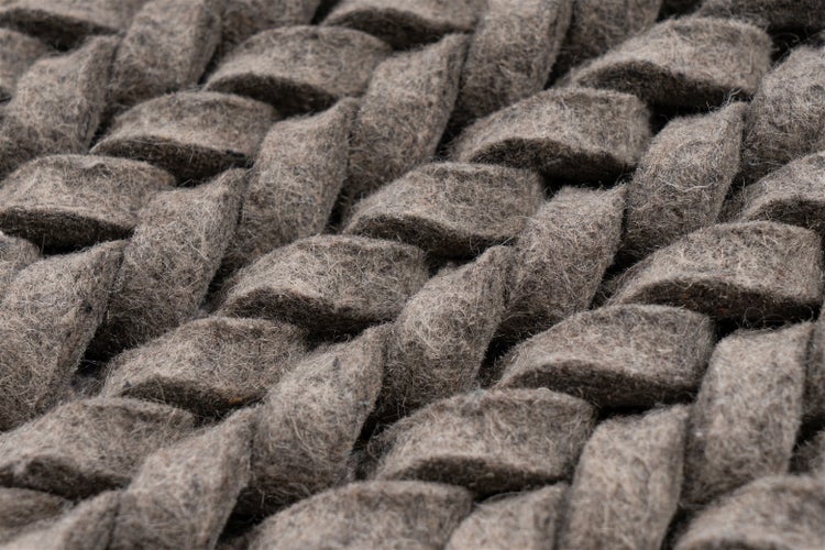 Detailní záběr na pletený plstěný koberec s hrubou strukturou a silnou vazbou.