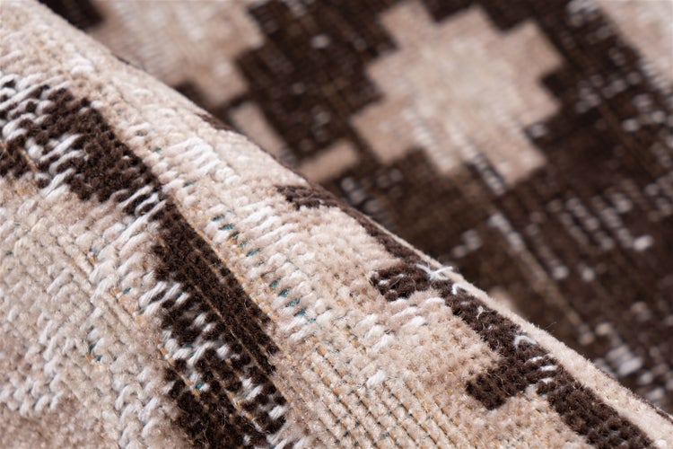 Detailní záběr tkaného koberce v hnědé a béžové barvě s geometrickým vzorem a jemnou texturou.