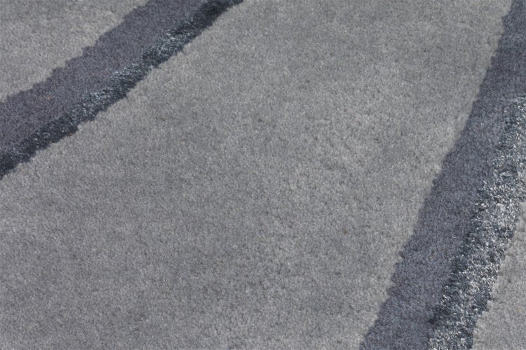 Detail mekkeho koberce s sedym vlnitym vzorem a tmavymi pruhy.