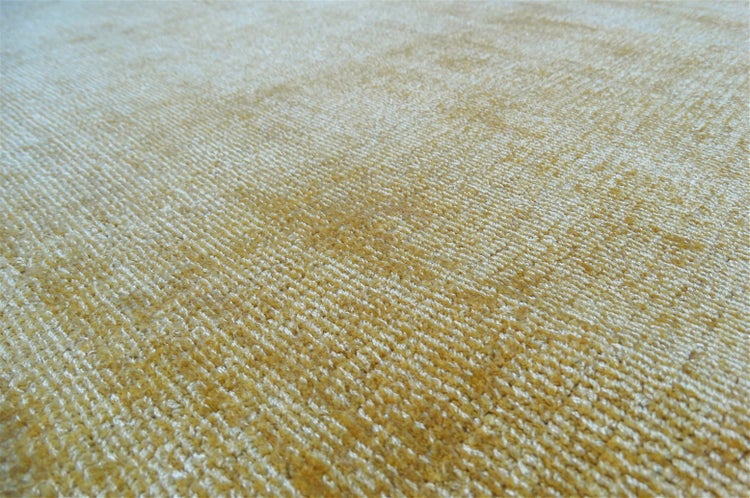 Detailní záběr na zlatý koberec s jemnou žebrovanou povrchovou strukturou.