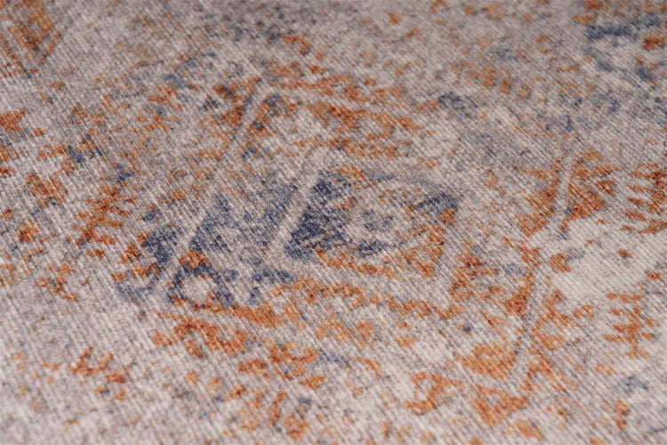 Detail strukturovaného koberce s vybledlým vintage vzorem v modré a terakotové barvě.