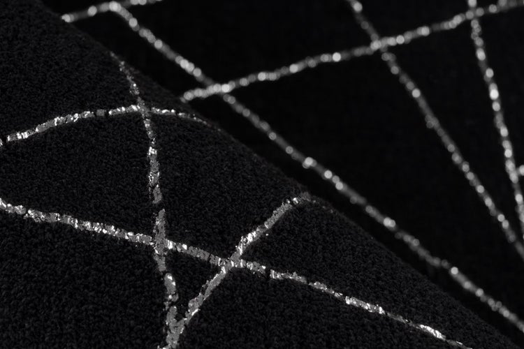 Detailní záběr černého koberce se stříbrným geometrickým vzorem linií a měkkou texturou.