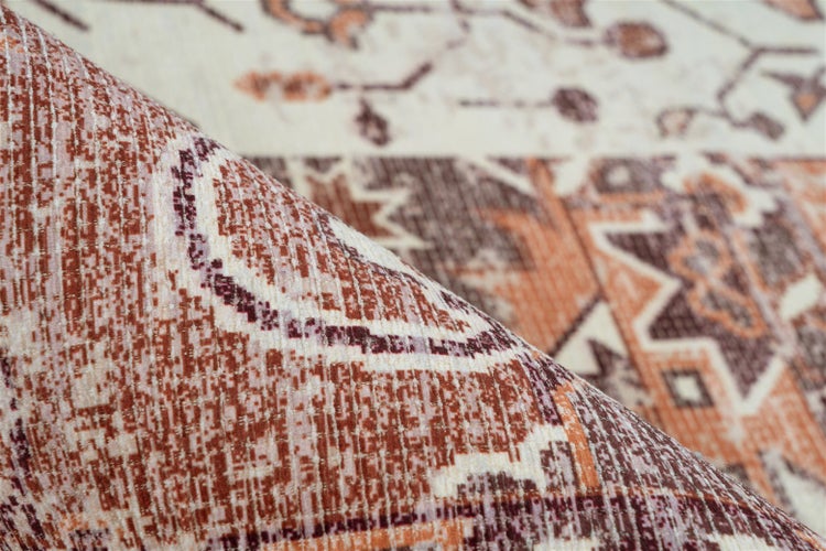 Detailní záběr tkaného koberce s orientálním geometrickým vzorem a ohrnutým okrajem.