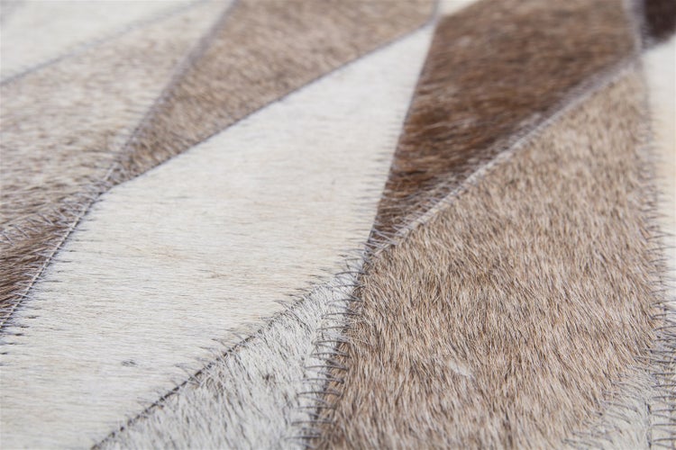 Detailní záběr koberce z pravé hovězí kůže v patchworkovém stylu s geometrickými vzory a viditelným prošíváním.