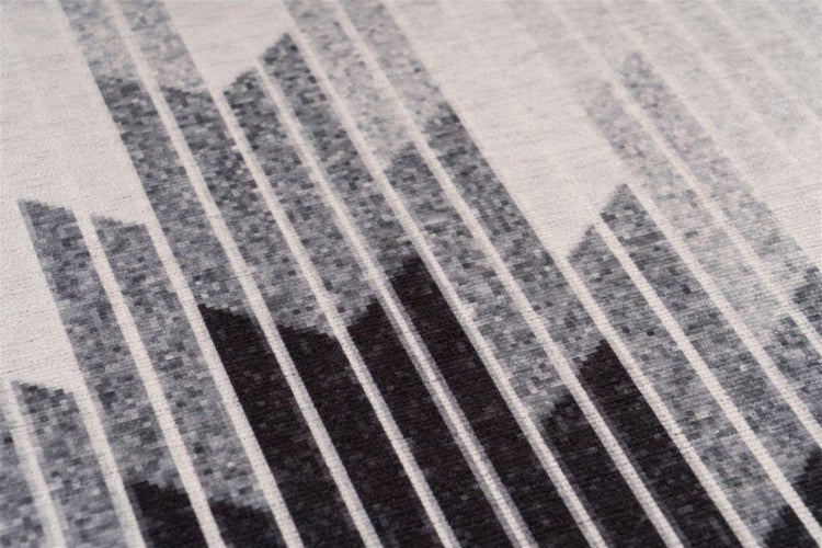 Detail koberce s geometrickým vzorem linií. Tkaná textura se svislými pruhy v odstínech šedé.