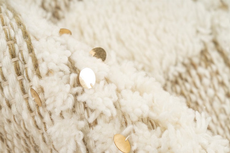 Detailní pohled na hrubě tkaný textil s dekorativními kovovými flitry.