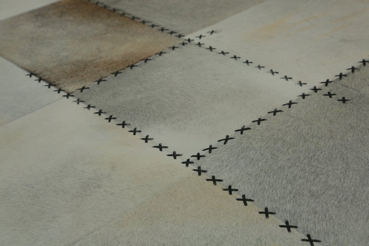 Detailní pohled na patchworkový koberec z hovězí kůže s viditelnými křížkovými stehy mezi čtvercovými kusy kůže.
