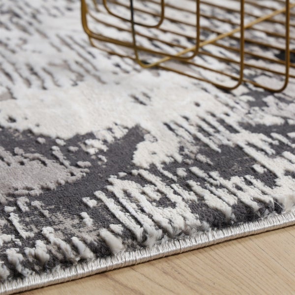 Detail strukturovaného koberce s šedo-bílým abstraktním vzorem na dřevěné podlaze.