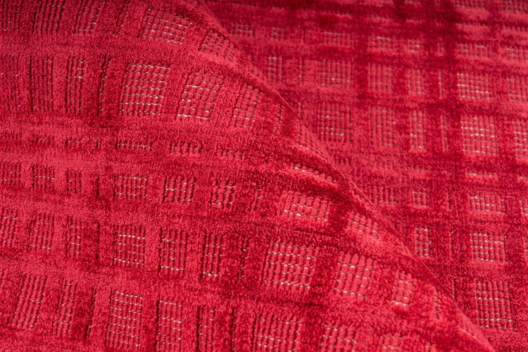 Detailní pohled na červený koberec s texturovaným čtvercovým vzorem a ohrnutým okrajem.