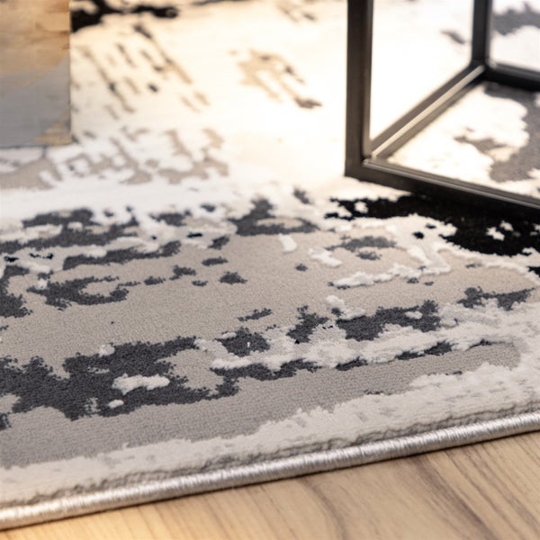 Detailní záběr na koberec s nízkým vlasem a abstraktním vzorem v šedé a černé barvě na dřevěné podlaze.