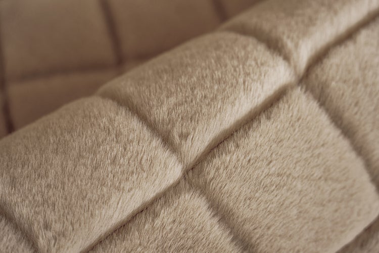 Detailní záběr na měkkou, béžovou plyšovou látku se čtvercovým prošívaným vzorem.