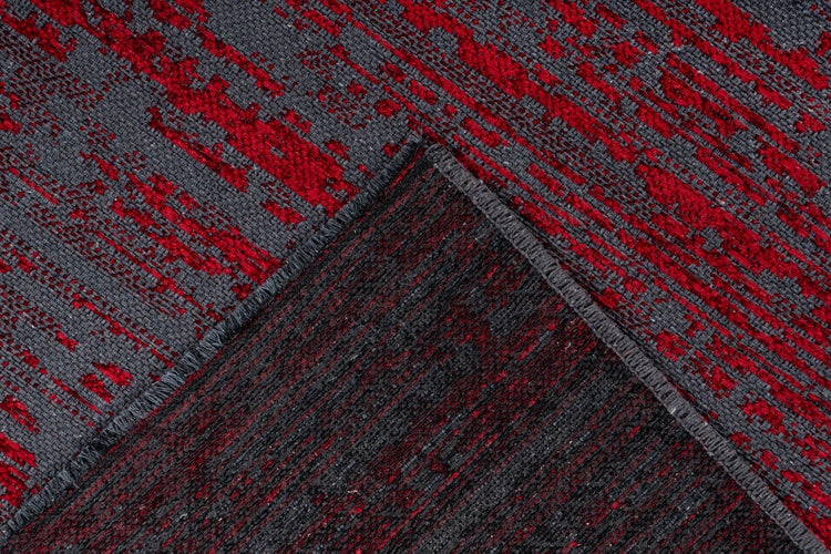 Detailní záběr červeno-šedého koberce s abstraktním vzorem, tkanou texturou, obšitým okrajem a spodní stranou.