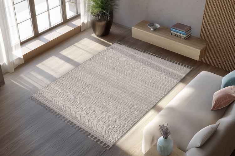 Obývací pokoj s tkaným kobercem s texturou a třásněmi, umístěným na světlé dřevěné podlaze před pohovkou a moderní komodou.