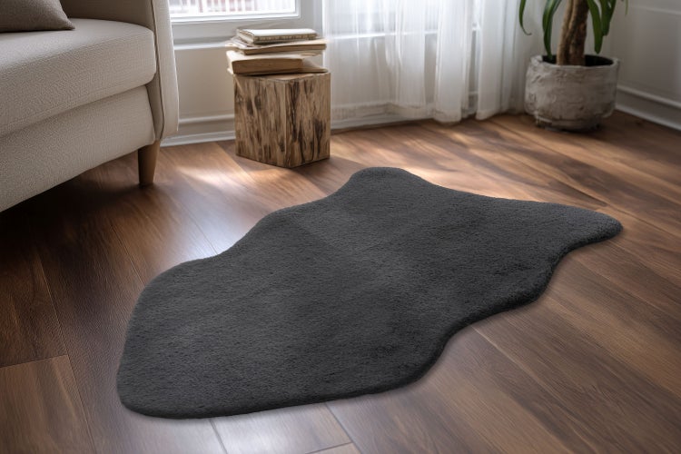 Nadýchaný koberec z umělé kožešiny v organickém tvaru na dřevěné podlaze v útulném pokoji.
