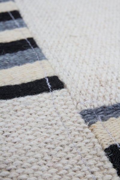 Detail tkaného koberce s pruhovaným vzorem a hrubým, strukturovaným povrchem.