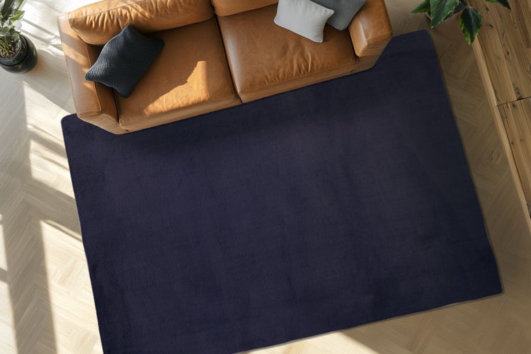 Tmavě modrý obdélníkový koberec do obývacího pokoje před koženou pohovkou na dřevěné podlaze v moderním interiéru.