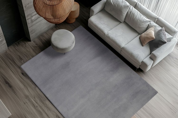 Moderní obývací prostor při pohledu shora s velkým obdélníkovým kobercem, pohovkou a kulatým taburetem na dřevěné podlaze.