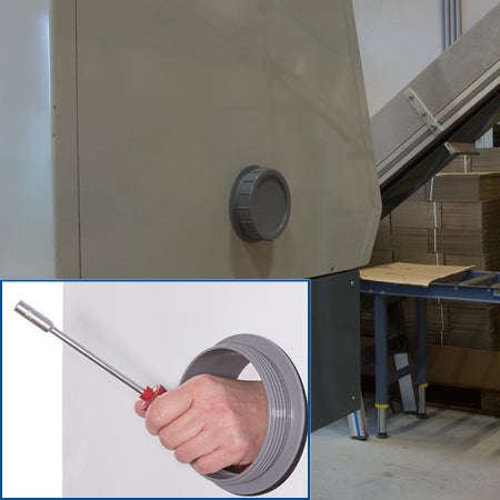 Šedý revizní uzávěr na průmyslovém stroji, detailní pohled ukazuje ruku s nástrojem v kruhovém servisním otvoru.
