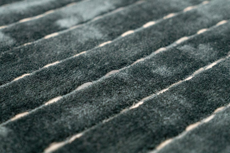 Detailní záběr měkkého koberce s žebrovanou povrchovou strukturou a světlými liniemi.