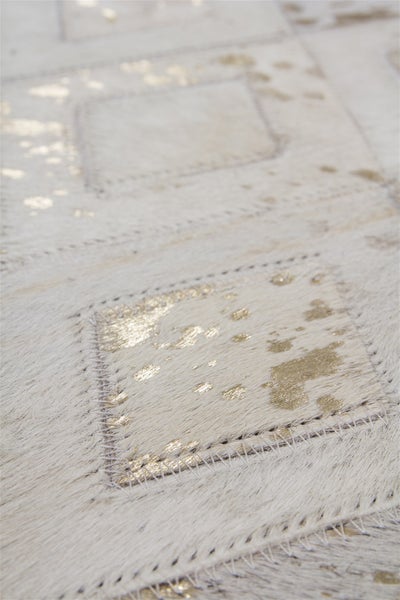 Detailní záběr na koberec z hovězí kůže v patchworkovém designu se zlatými prvky a viditelnými švy.