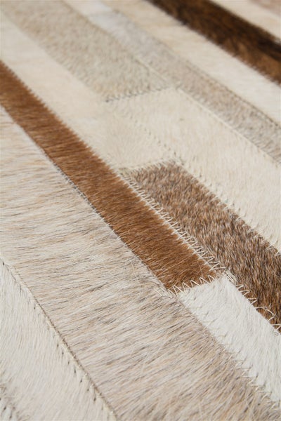 Detailní pohled na patchworkový koberec z pravé hovězí kůže s viditelným prošíváním v odstínech hnědé a béžové.