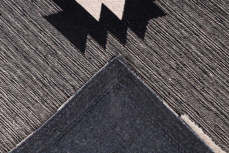 Detail tkaného koberce v černo-bílé barvě s geometrickým vzorem a strukturovanou zadní stranou.