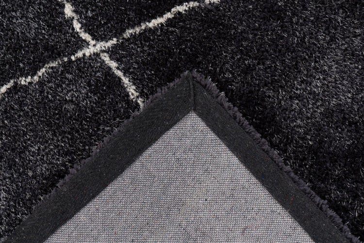 Detail černého koberce s vysokým vlasem s bílým geometrickým vzorem a viditelnou zadní stranou.
