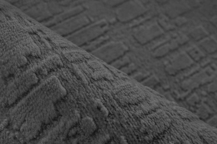 Strukturovaný koberec s geometrickým reliéfním vzorem v detailu.