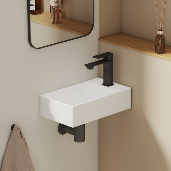 Moderní toaleta pro hosty s bílým obdélníkovým nástěnným umývátkem, černou baterií a černým sifonem v minimalistickém designu.