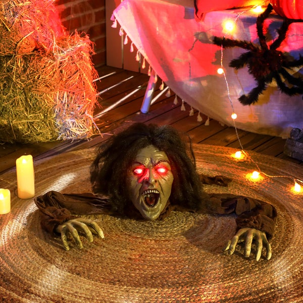 Dekorativní halloweenská scéna s figurkou zombie, balíky sena a světly.