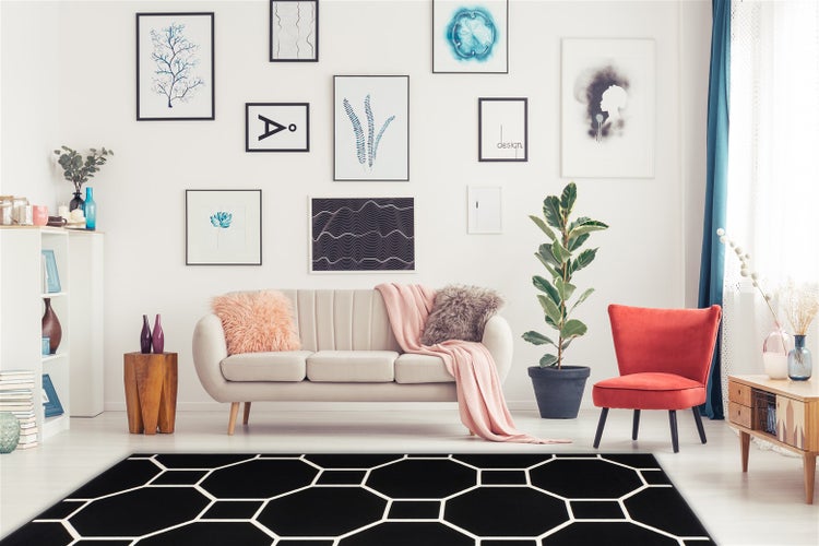 Moderní obývací pokoj se světlou pohovkou, červeným křeslem a výrazným černým kobercem s geometrickým vzorem na podlaze.