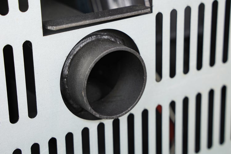 Detailní pohled na připojení kouřovodu na kovové zadní stěně krbových kamen s ventilačními otvory