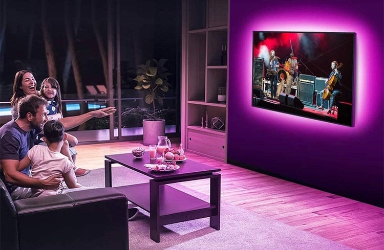 Rodina v obývacím pokoji sleduje televizi s atmosférickým LED podsvícením pro pohlcující zážitek z domácího kina.