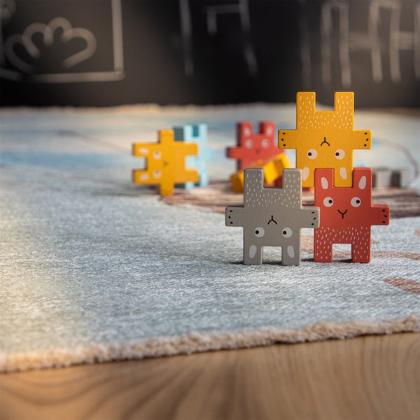 Stohovatelné dřevěné figurky ve tvaru zajíčků na dětském koberci pro kreativní hraní.