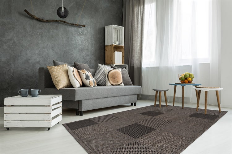 Detailní záběr na tkaný koberec s geometrickým vzorem v hnědé a černé barvě.