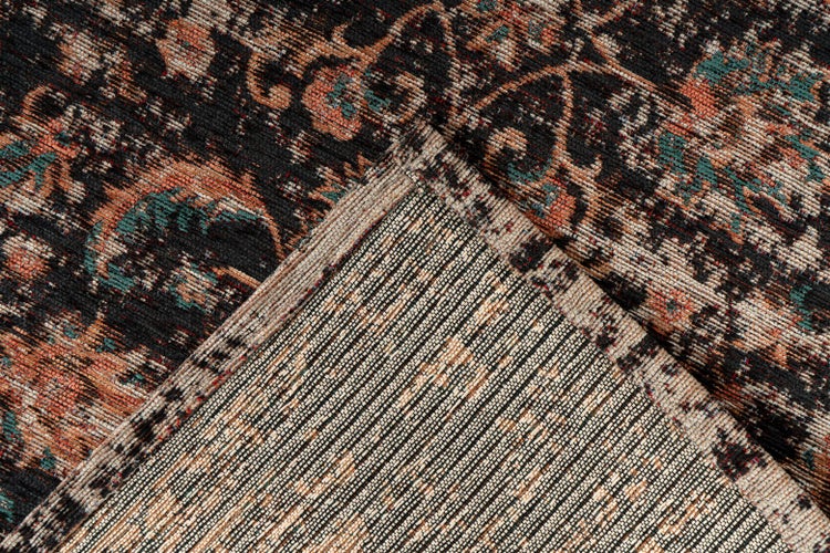 Detail koberce s vintage vzorem a ohrnutým rohem, který ukazuje strukturovanou zadní stranu.