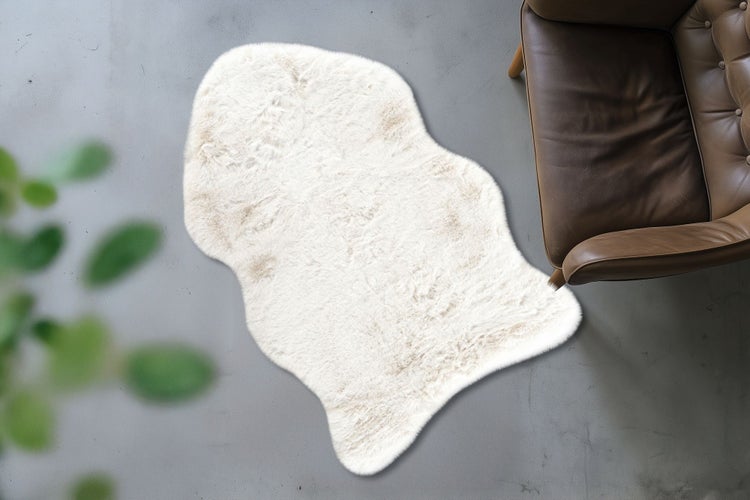 Kvalitní koberec z imitace ovčí kůže v organickém tvaru na podlaze vedle koženého křesla.