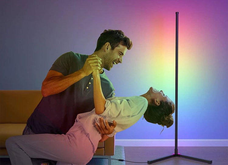 Pár tančí v obývacím pokoji vedle moderní, štíhlé LED stojací lampy, která na stěnu vrhá atmosférické RGB světlo.