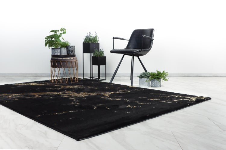 Moderní černý koberec se zlatými detaily v elegantně zařízeném obývacím pokoji se židlí a rostlinami.