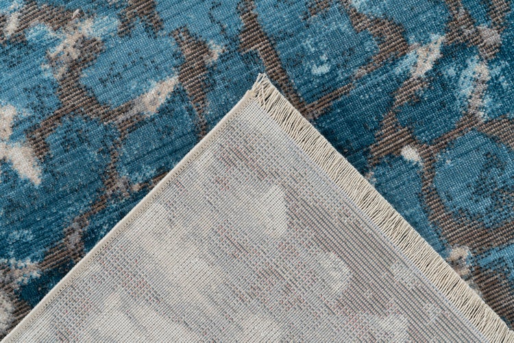 Detailní záběr koberce s abstraktním vintage vzorem, přehnutý roh ukazuje tkanou zadní stranu a třásně.